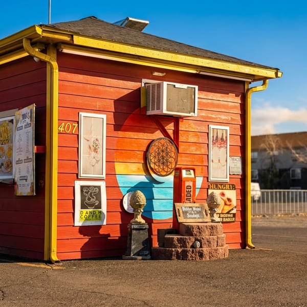 Red restaurant building with yellow trim, walk-up windows displaying menus, and decorative wall art.