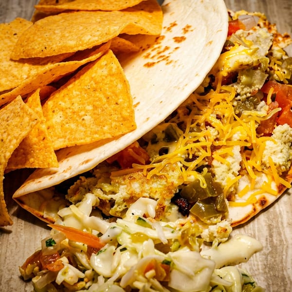 Breakfast taco with scrambled eggs, cheese, and vegetables, served with tortilla chips and coleslaw.